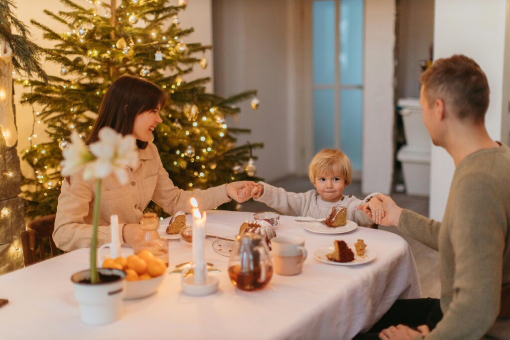 a family siting around a table with a christmas tree and holiday lights in the background